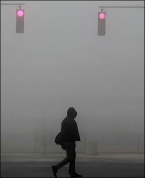 Aaron Pettaway makes his way across North St. Clair Street in a heavy fog at the end of the workday. Wednesday was unusually warm too.