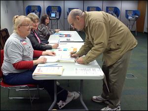 Merlin Artz signs in to vote Tuesday morning at Perrysburg precinct 690 with pollworker Stephanie Hennigan, of Perrysburg, left as pollworkers Diane Markham, of Perrysburg Township, second from left, and Mary Kurtz, of Custar, look on.