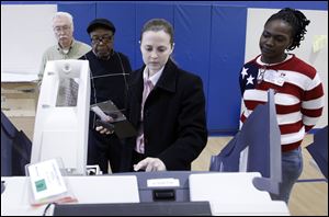 Meghan Gallager, director of the Lucas County Board of Elections, works on a voting machine at Sherman Elementary School in Central Toledo as poll worker Lance Wehrle, left, and presiding judges Theo Washington and Shareta Lewis observe.