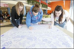 Courtney Brecher, left, a junior from Cleveland, Lucy Sherman, center, a freshman from Vandalia, and Ariel Jones, right, a senior from Sylvania, sign memory boards that are set up in the BGSU student union for people to leave thoughts and condolences for the families of the three sorority girls killed by a wrong-way driver and for the two girls who survived the crash.  

