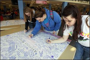 Bowling Green State University students Courtney Brecher, left, Lucy Sherman, and Ariel Jones sign memory boards set up at the BGSU Student Union.