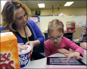 Lauren Miller, speech-and-language pathologist, helps Joselyn 'Jo' Johns, 6, pick a snack during kindergarten at Fort Meigs Elementary School. She began using the device earlier this month.