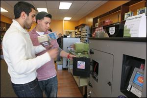Sales and marketing director Chris Markho, left, shows customer Justin Lusher how to prepare a machine to make cigarettes at the RYO Filling Station at Tobacco Haven on Spring Valley Drive in Holland.