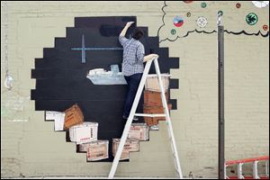 Halal Mohamed’s paints a mural Tuesday on a wall of Thomas Porter Architects on North St. Clair Street downtown.