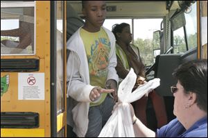 Seventh grader Deontez Powell assists with distributing bags of free food for students to take home on a bus outside Roll Hill Elementary School in Cincinnati.