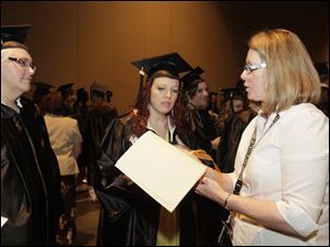 Bachelor of Arts in the Science of Nursing [B.S.N.] graduates Rebecca McCann, of Adrian, Michigan, left, and Erin Marten-Snyder, of Toledo, are checked off before the procession by Lourdes University employee Kathie Myers, of Waterville.  