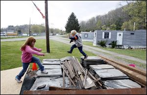 At left, Steve McGrath watches as his daughter, Cheyenne McGrath, 5, and Dallas Snyder, 5, play on a stack of scrap stone that Mr. McGrath plans to sell for extra money. ‘I buy and sell cars, do demo work, do what I can … I’m just a handyman trying to make it,’ he said.