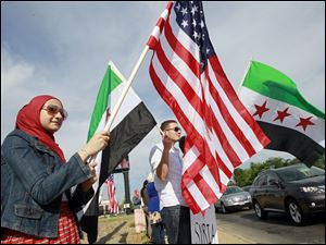 Sylvanian Zaynab Alfaham flies the U.S. flag as Anwar Saleh, also of Sylvania, waves a Syrian flag from the early ’60s at a West Toledo rally for Syrian freedom. About 40 people participated Friday at Talmadge Road and Sylvania Avenue.