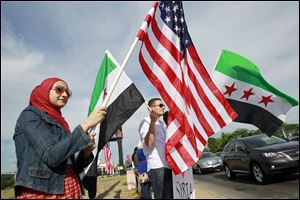 Sylvanian Zaynab Alfaham flies the U.S. flag as Anwar Saleh, also of Sylvania, waves a Syrian flag from the early ’60s at a West Toledo rally for Syrian freedom. About 40 people participated Friday at Talmadge Road and Sylvania Avenue.