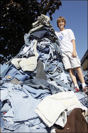 Erek Hansen of Curtice, Ohio, stands on a pile of jeans. His goal is to send 5,000 pairs to Cotton: From Blue to Green, a group that collects denim to recycle into housing insulation.