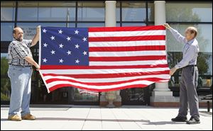 Tom Apel, left, and Richard Baranowski display a 15-star flag to be raised during a Monday ceremony at Perrysburg’s Way Public Library to commemorate the beginning of the War of 1812.