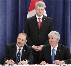 Canadian Prime Minister Stephen Harper watches Canada's Transport Minister Denis Lebel, left, and Michigan Gov. Rick Snyder sign an agreement for the construction of a new international bridge between Detroit and Windsor, Ontario.