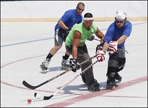 Nate Ackerman of the Golddiggers, center, and Shane O’Brien, right, of Mick Electric battle for the ball as Mr. O’Brien’s teammate, Danny Kroggel, trails them during a Toledo Street Hockey League game Sunday at the Ottawa Park ice rink in Toledo. The league, which was formed in 2008, consists of 28 teams with about 300 players and has been using the rink for its games for the last three years.