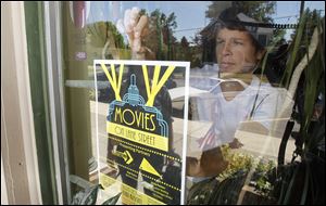 Levi Makula, a Blissfield High School student, places a poster promoting the movie night in a shop window on South Lane Street.