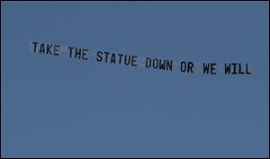 A plane flying over the Penn State University campus in State College, Pa., pulls a banner reading 'Take the statue down or we will'. The towing company is from Wood County, Ohio.
