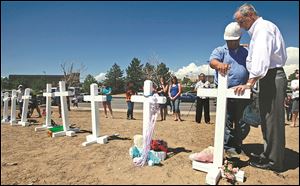 Steve Hogan, right, mayor of Aurora, Colo., where the movie theater attack took place, pauses to pray as Greg Zanis places a cross for the shooting victims. Mr. Zanis also placed crosses in 1999 for Columbine attack victims.