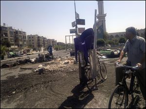 This citizen journalist image shows a man on a bicycle surveying a street damaged by tank treads after fighting between rebels and Syrian troops in the Yarmouk camp for Palestinian refugees in south Damascus, Syria. Rebel commanders in northern Syria vowed Sunday to liberate the country's largest city, Aleppo, from government control, and rebel forces seized a nearby army infantry school, a senior military defector in Turkey and rebel sources within Syria said.