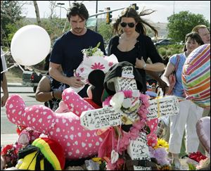 Actor Christian Bale and his wife Sibi Blazic view a cross and large display of flowers and stuffed animals dedicated to Veronica Moser-Sullivan, 6, the youngest of the 12 victims of Friday's mass shooting, Tuesday.