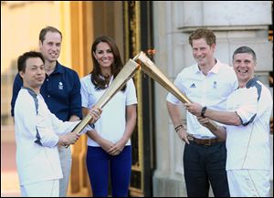 Prince William, his wife, Catherine, and Prince Harry watch Wai Ming Lee, from a charity of which Prince Harry is a patron, hand over the torch to John Hulse, of a charity of which Prince William is a patron, at Buckingham Palace.