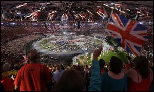 A spectator waves the Union Jack as fireworks light the sky over the Olympic Stadium. The city of London put on a 3-hour, 45-minute performance Friday night at a cost of about $42.5 million.