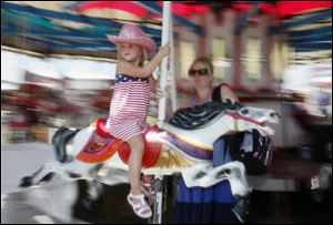 Ableen Carroll, 4, and mother, Crystal Carroll, of Haskins, Ohio, ride the merry-go-round at the fair in Bowling Green. For some, the fair with its animals, food, and rides is an inexpensive vacation.