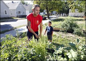 Brad Fields, an urban urban agriculture/landscape design student at Owens Community College, left, and little helper Martine Garcia, 5, right, pulls out a few weeds from his tomato patch in a community garden in Toledo.