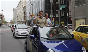 Jennifer Tyrrell, one of two grand marshals for the Toledo Pride parade, waves to the crowd as a rainbow of Fiat 500s travels forward. 