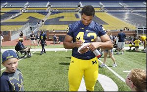 Whitmer High School graduate Chris Wormley, a defensive end for the team, signs a football on Fan Day at the University of Michigan. At left is Camden Dings, 7, of Toledo.