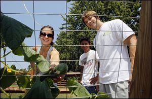 Meghan Yarnell picks a cucumber with Sammy Irias, center, and her husband, Andy Yarnell, in their backyard garden.
