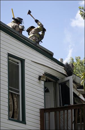 Members of the Toledo Fire Department work to open up the roof of a structure during a fire on North Michigan Street Friday.