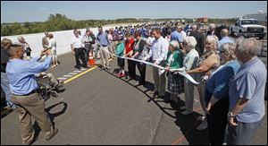 Spectators take turns posing with a ceremonial ribbon at the event, which drew about 200 dignitaries, including many who fought for decades to build an expressway.