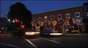 Vehicles drive by a mural representing local people by Bowling Green State University students in the 1200 block of Broadway in the Old South End.