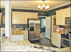 The kitchen’s antiqued  white cabinets and dark  walls make a perfect backdrop for the beautifully  veined granite countertop.