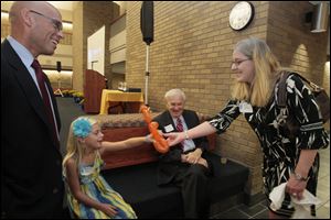Kim Renz hands a dog balloon to her daughter, Aubry, as Aubry’s father, Maj. Michael R. Renz, looks on. The dog was crafted by Rabbi Alan M. Sokobin, seated, who, with Major Renz, was among six honorees at the 2012 Law Awards reception Saturday at the University of Toledo.