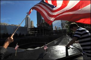 An American flag flies over a man pausing near a reflecting pool at the National September 11 Memorial during the observance of the 11th anniversary of September 11 in New York.