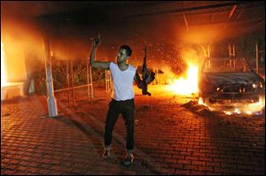 An armed man waves his rifle as buildings and cars are engulfed in flames after being set on fire inside the U.S. consulate compound in Benghazi.