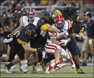 St. Francis De Sales High School player Michael Wagner is swarmed by Whitmer High School defenders Jack Linch, 44, Devin Thomas and Marquise Moore, 91, during the second quarter Friday at Whitmer High School.