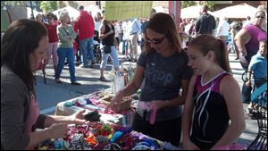 Melissa Lewicz, center, of Perrysburg and her daughter Bailey, right, look over the hair bows made by Sara Young at Harrison Rally Day on Saturday in downtown Perrysburg. Ms. Young sells baby accessories and shower gifts through her business Raining Babies.