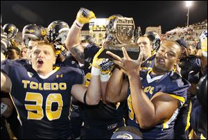 University of Toledo players including Ben Pike, 30, and Danny Farr, 92, holding Battle of I-75 trophy. Toledo celebrated after beating Bowling Green 27-15 at the Glass Bowl.
