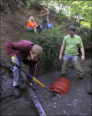 Alex Kurtz, left, a University of Toledo student, dislodges a barrel from a creek at Camp Miakonda under the observation of Kyle Spicer, project coordinator for Partners for Clean Streams.
