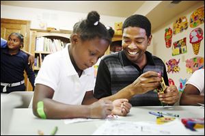 Stephen Draper, 27, laughs as Kashmere Watson, 6, tries to finish her coloring before Draper can place all the crayons back into their box at the Moody Manor Reading Room in Toledo.