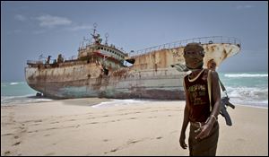 Masked Somali pirate Abdi Ali stands near a Taiwanese fishing vessel that washed up on shore after the pirates were paid a ransom and released the crew, in the once-bustling pirate den of Hobyo, Somalia.