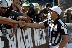 Referee Ed Hochuli (85) greets Oakland Raiders fans before an NFL football game against the Seattle Seahawks in Oakland, Calif. The NFL and referees' union reached a tentative agreement on Wednesday.