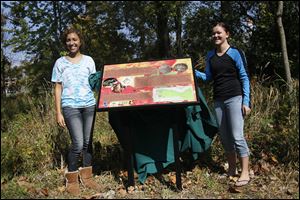 Rahma Ismail, 18, left, and Katie Dorsey, 17, beam as they display the sign at Harroun Community Park designed by students at Northview High School.