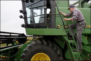 Douglas Pratt, 79, climbs into his combine to harvest a field of soybeans on his 400 acres in Perrysburg Township. Still, he acknowledges, a lot of people are hurting.