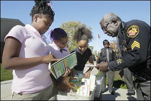Ella P. Stewart Academy for Girls sixth graders Najae Pettaway, left, Taylor Hughes, and Jayona Wren search through some of the books brought to the school by Lucas County sheriff's Deputies E.L. Linzy, right, and Valerie Hughley, background.