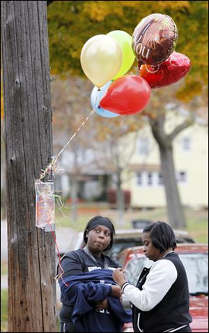 Nikira Weathers, left, looks at a picture of Deontae Allen, as Vena Reynolds tapes it down where Allen, 19, was shot and killed Thursday night in the 1400 block of Waverly Avenue.