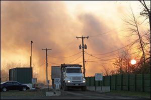 A truck leaves the Stickney Recycling plant on Creekside Drive in Toledo, as smoke from a fire on the grounds obscures the rising sun, Thursday.