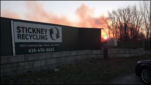 The sun rises behind Stickney Recycling Plant, as a fire smolders in the distance.