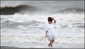 A beach goer holds on to her hat as she walks along a breezy Coligny Beach Park on Hilton Head Island, S.C., watching the waves generated by Hurricane Sandy near the time of high tide on Saturday morning.